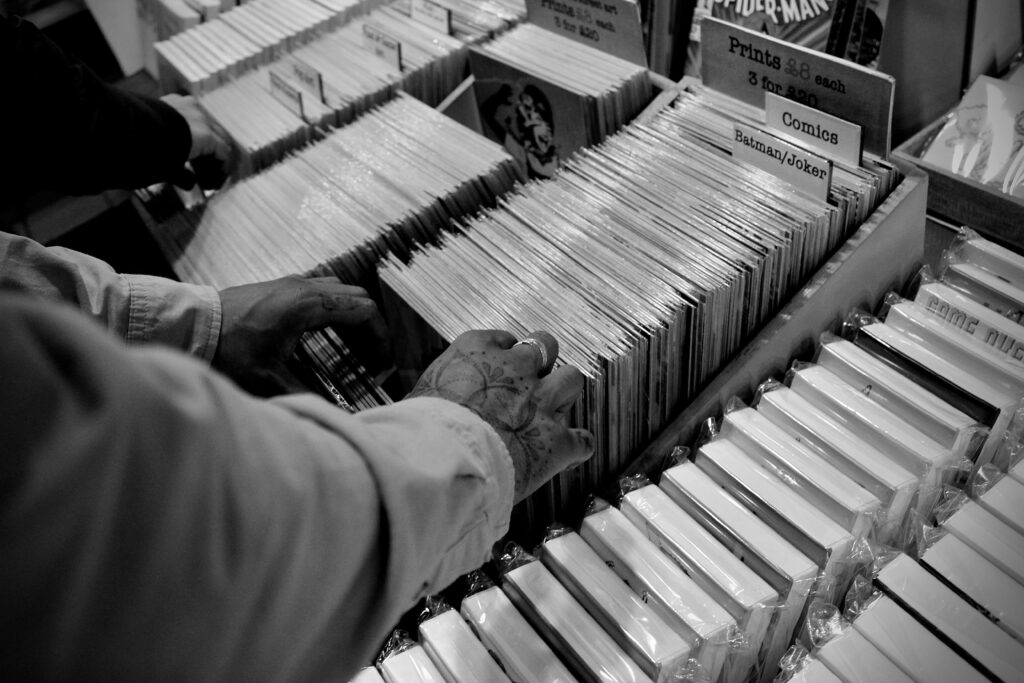 Monochrome image of a person browsing comic books in a store, showcasing comics and vintage prints.